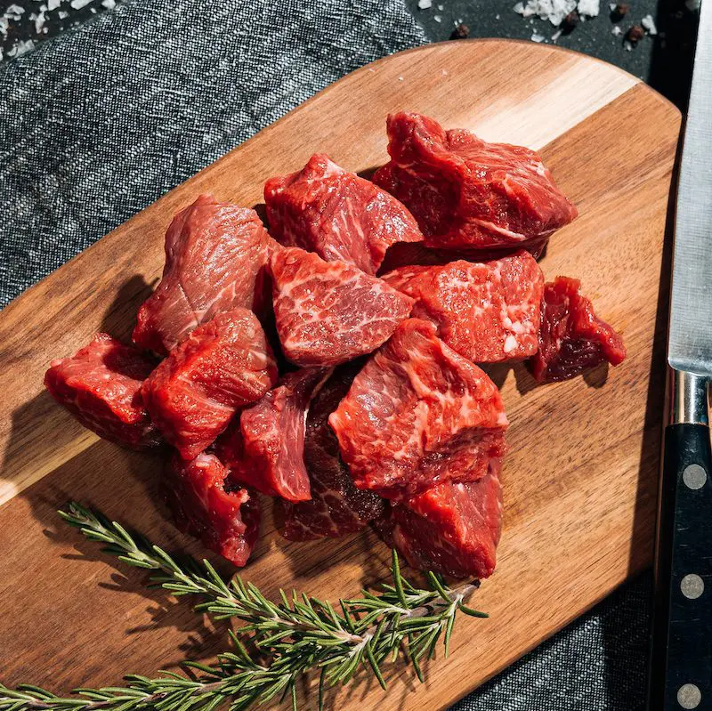 square cuts of raw steak on cutting board for stew